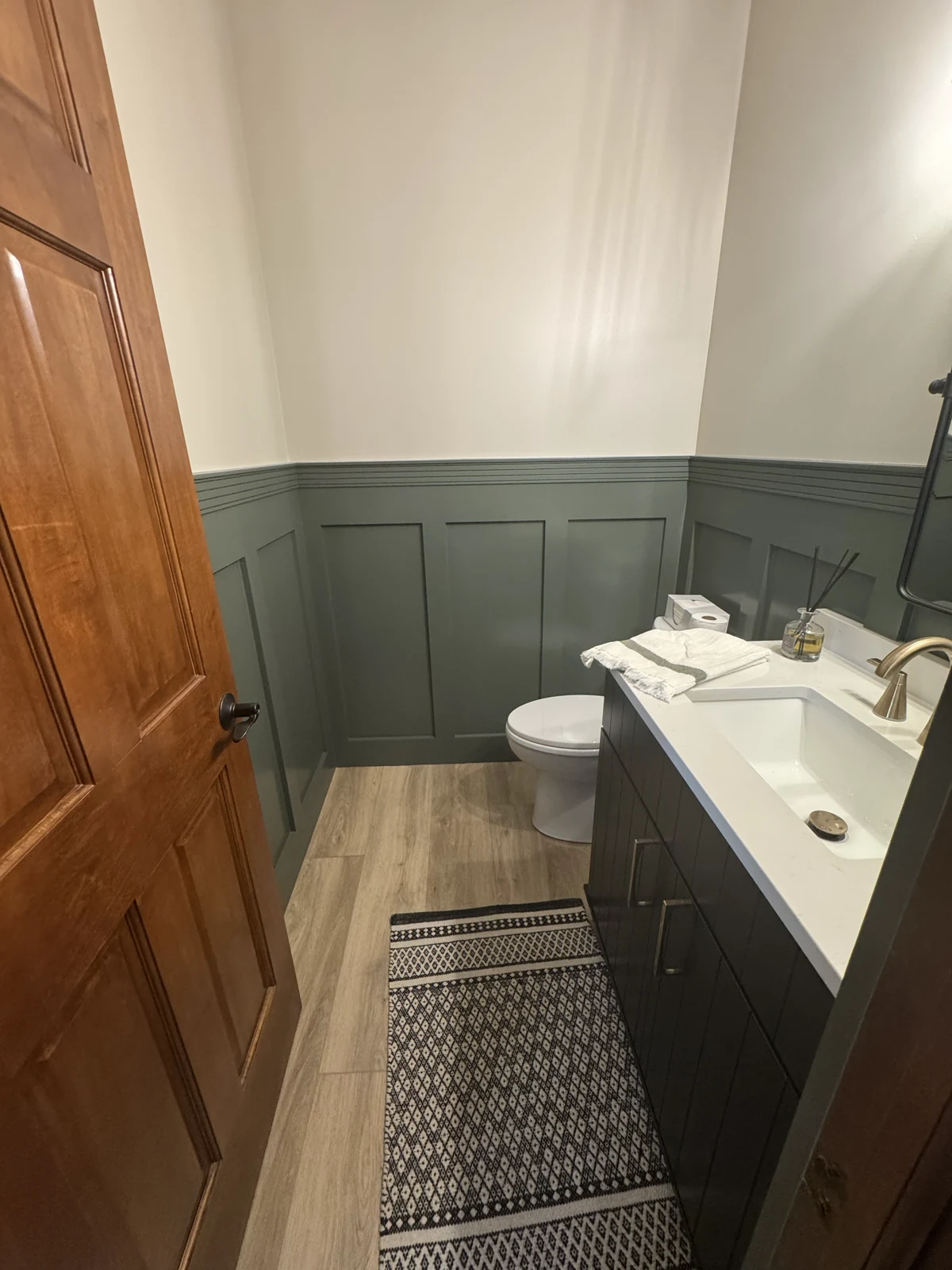 Completed hall bathroom with green wainscoting and a compact vanity