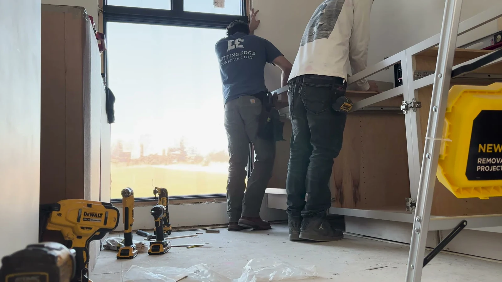 Cutting Edge crew fitting white base cabinets beside a large window in the DeSoto home