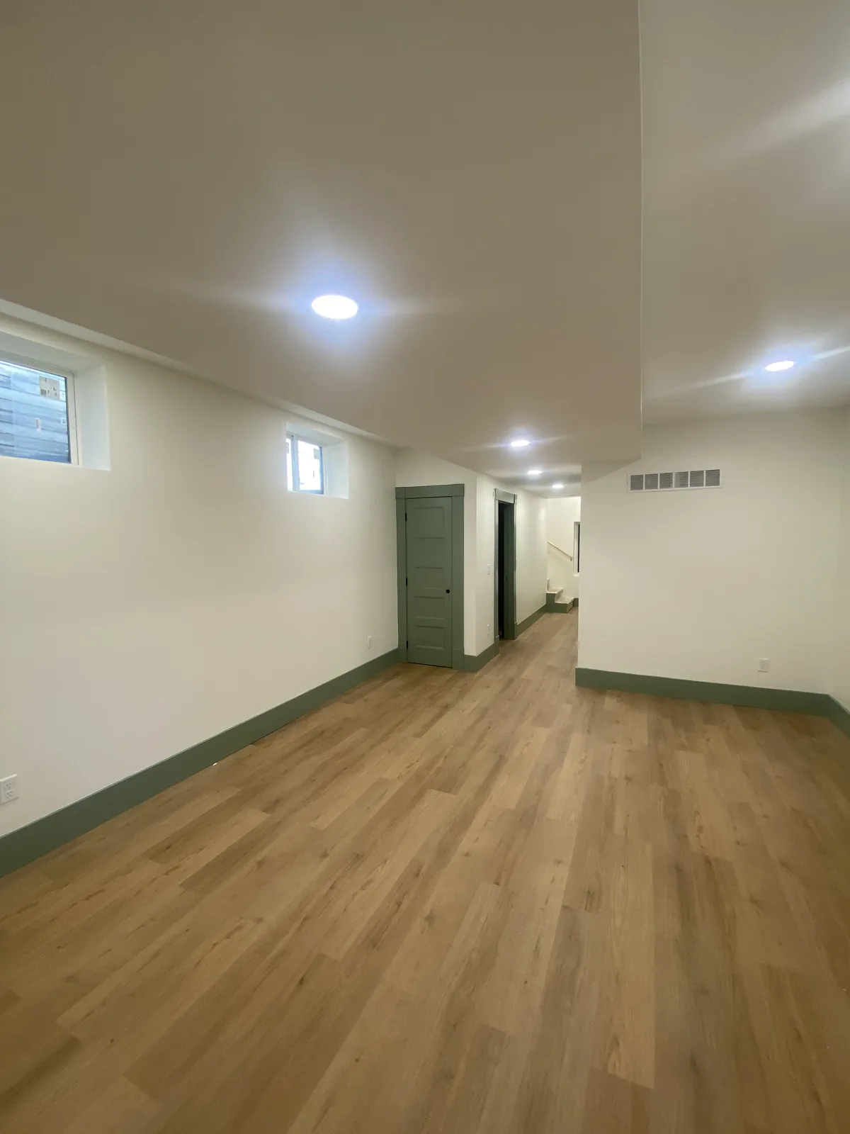 Finished lower-level room with green trim and wood-look flooring
