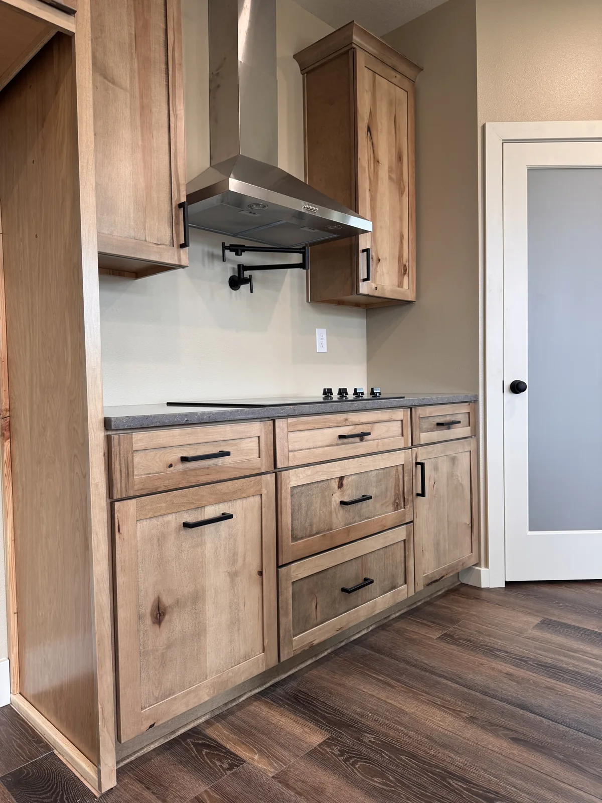 Finished natural wood kitchen cabinetry with a stainless steel hood